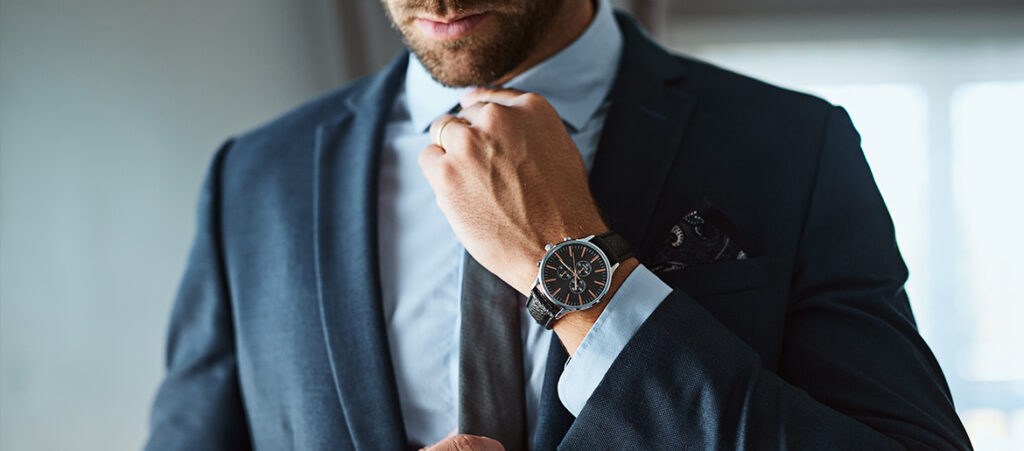 Mężczyzna w garniturze z zegarkiem na ręce poprawia krawat