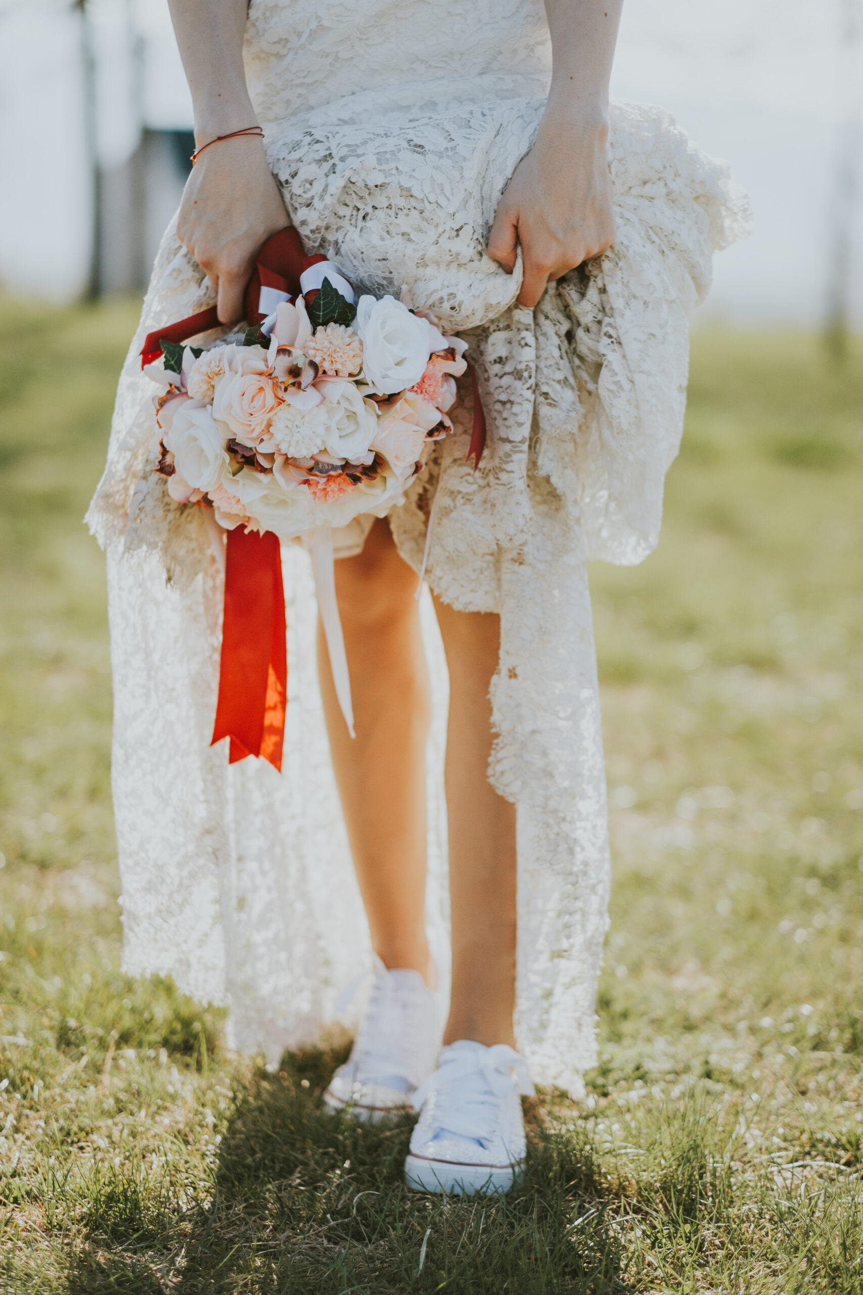 Γυναίκα με boho νυφικό με λουλούδια στο χέρι και χαμηλά λευκά sneakers στα πόδια