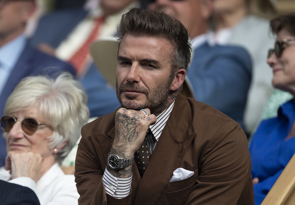 Davidas Beckhamas, dėvintis rudą švarką ir dryžuotus marškinius