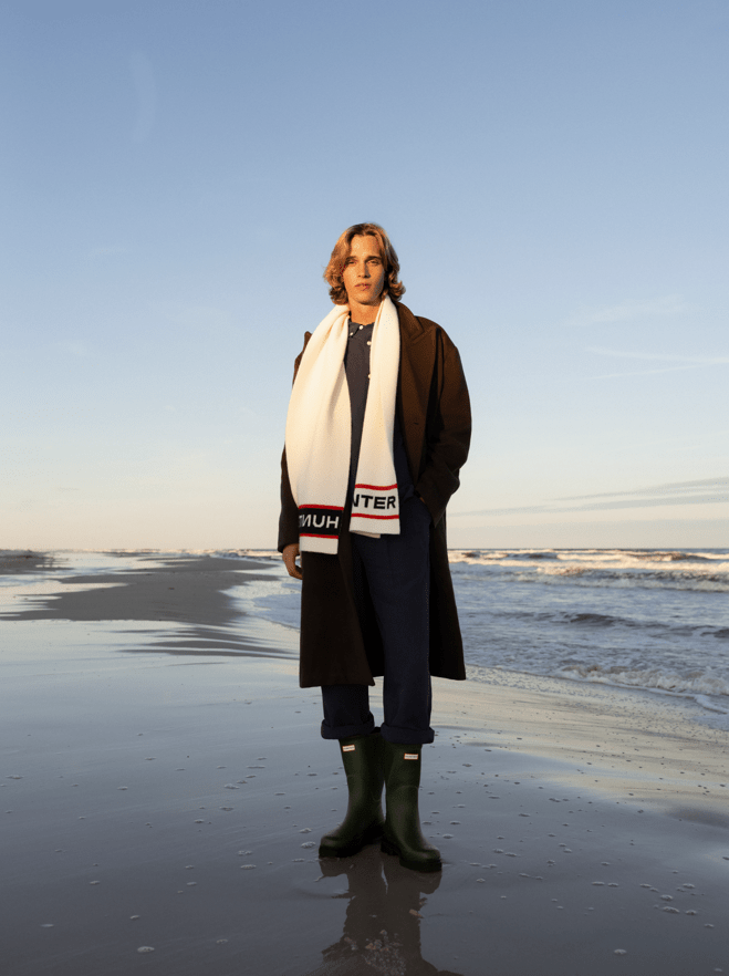 Hunter gumicsizmát és sálat viselő férfi a tengerparton